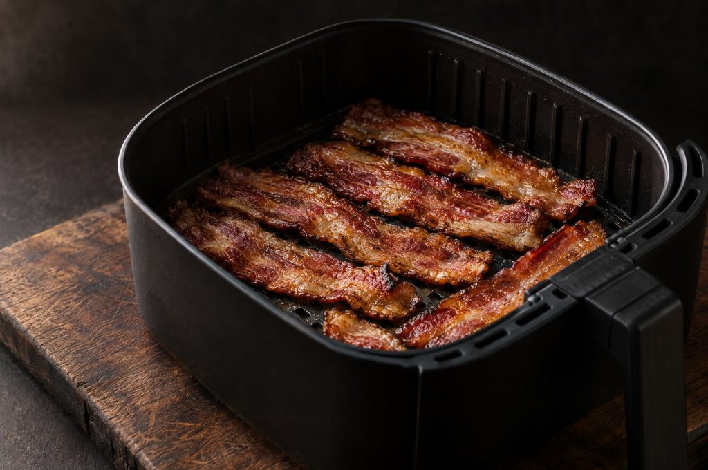 Air fryer bacon: crisp thick cut bacon slices in a single layer in a black air fryer basket set on a dark walnut board